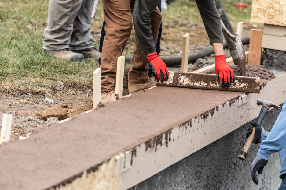 Workers leveling freshly poured concrete in wooden forms for a sidewalk or concrete slab at a construction site.